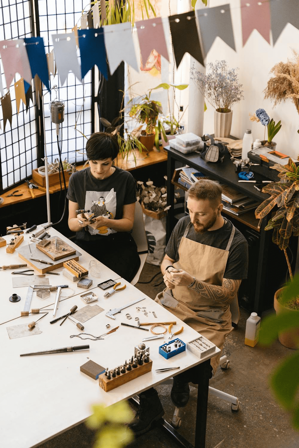 Two jewellery makers working on handcrafted pieces in a decorated workshop.