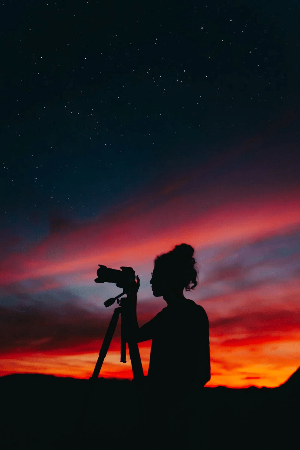 Photographer silhouetted against a vibrant sunset sky using a tripod camera.