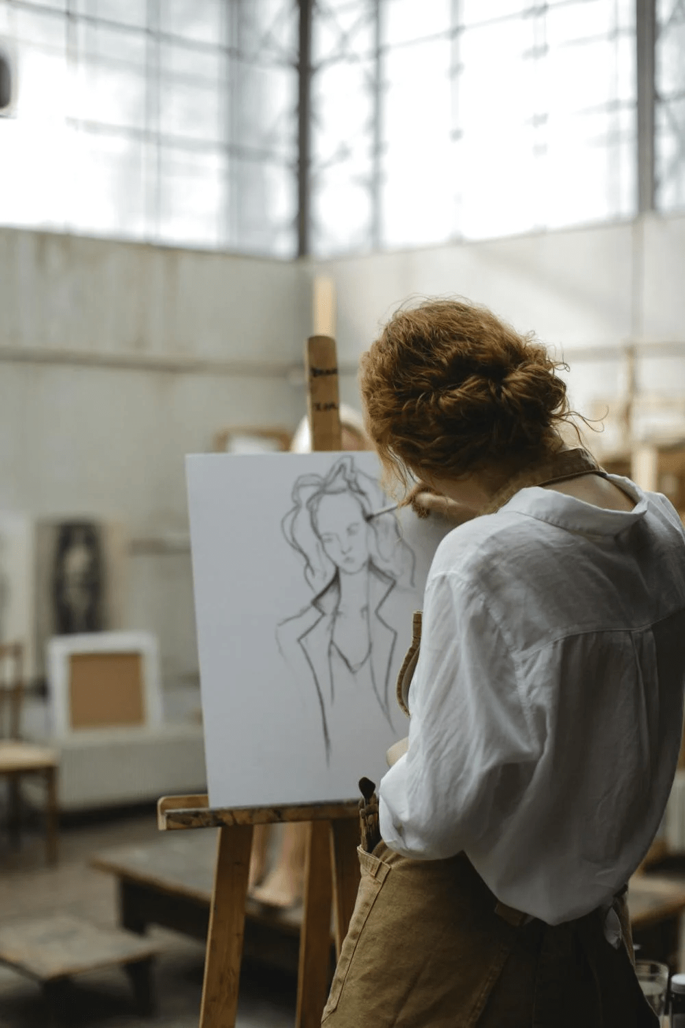 Artist sketching a portrait on an easel in a bright art studio.
