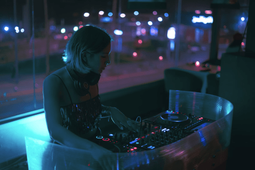 Female DJ performing at an event using a DJ mixer in a dimly lit venue.