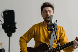 Male musician playing guitar and singing into a microphone during a recording session.